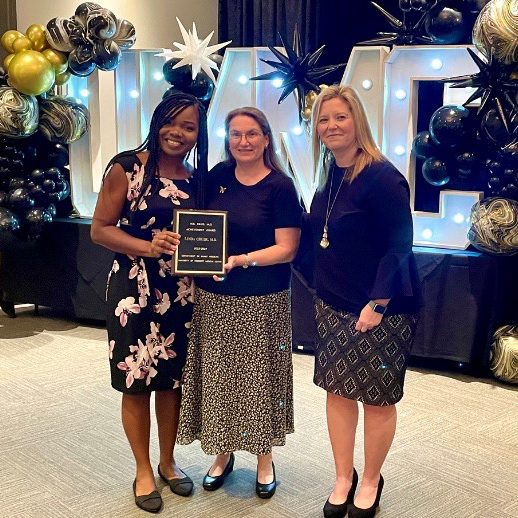 Linda Chude stands with two faculty members holding an award.